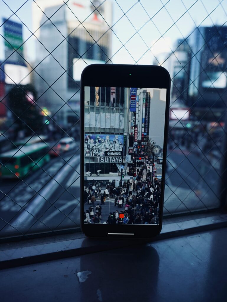 A smartphone captures a bustling city street scene viewed through a window grid.
