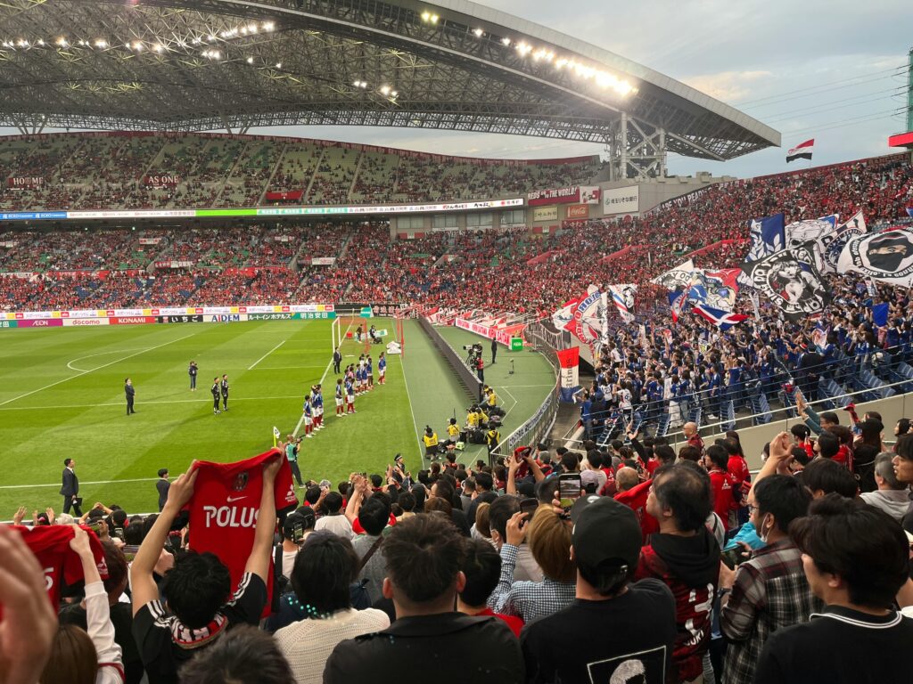 Energetic crowd cheering at a soccer match in Saitama Stadium, Japan.